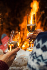 Back view of couple enjoying and celebrating together clinking with champagne flutes inside home with fireplace in background. Winter holiday season and love in relationship. Anniversary new year eve