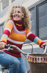 Happy middle age active woman riding a bike in the city wearing colorful sweater. Green transport...