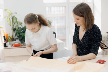 Smiling small girl dressmaker. Child use scissors for cutting fabric, sewing master class in school