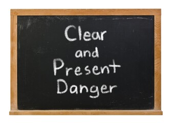 Obraz premium Clear and present danger written in white chalk on a black chalkboard isolated on white