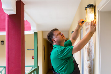 Fototapeta na wymiar A man repairs a lamp in the hallway front of the house.