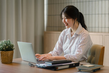 Smiling young asian businesswoman using laptop to work online, remote work.