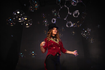 Magician illusionist woman in red costume performing soap bubbles show, happy look. Chic circus...