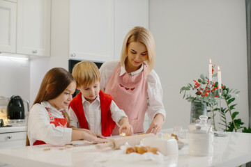 Obraz na płótnie Canvas Happy mother with children cutting different shapes of cookies in the kitchen. Mother with daughter and son are making Christmas cookies at home and having fun.