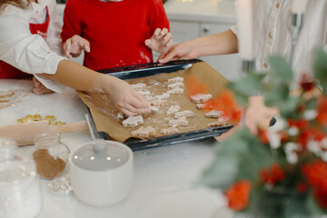 Obraz na płótnie Canvas A mother with her daughter and son prepares Christmas cookies, children put cookies on a baking sheet. Close up.