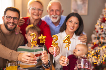Multi-generation family holding balloons shaped as numbers 2024 while having Christmas dinner