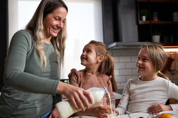 Sweet morning ritual: Mother and daughters joyfully spreading jam on bread, savoring the simple delight of a shared, sweet breakfast. 