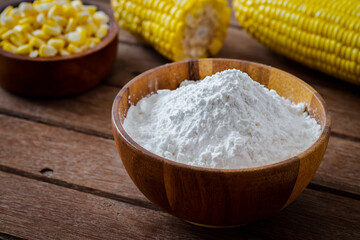 Fototapeta na wymiar Corn flour in wooden bowl and corn cobs on table