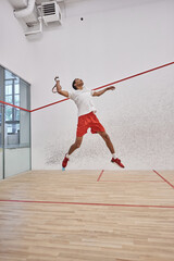 motion shot, energetic african american player holding racquet while jumping and playing squash