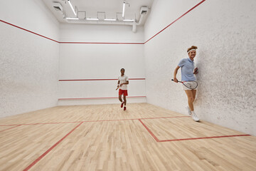 dynamic interracial players playing squash together inside of court, challenge and motivation