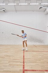 young redhead sportsman in headband playing squash inside of court, challenge and motivation