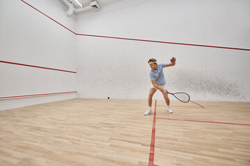 young and active redhead man in sportswear playing squash inside of court, challenge and motivation