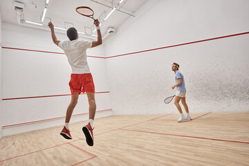 interracial players in sportswear jumping and playing squash inside court, challenge and motivation