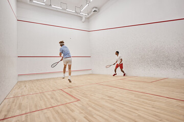 athletic interracial men in sportswear playing squash inside of court, challenge and motivation