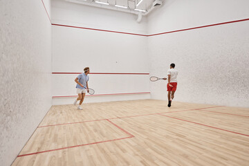 active interracial sportsmen in sportswear playing squash inside of court, challenge and motivation