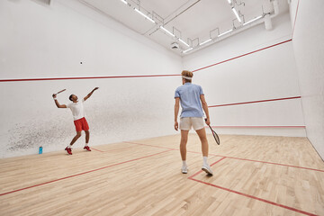 Fototapeta na wymiar athletic and diverse men in sportswear playing squash together inside of court, motivation