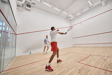 multicultural athletic men in sportswear playing squash together inside of court, motivation