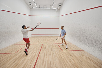 multicultural men in sportswear playing squash together inside of court, motivation and sport