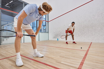 tired interracial friends in sportswear breathing heavily after playing squash in court, motivation
