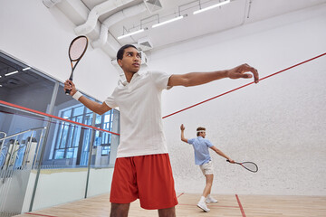 interracial players in sportswear playing squash together inside of court, active lifestyle