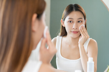 Happy beauty, attractive asian young woman, girl looking reflect in mirror, hand holding cotton pad, applying facial wipe on her face remover makeup, essence or lotion for treatment, skin care routine