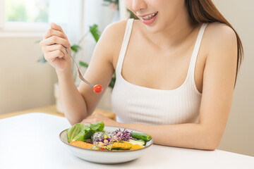 Diet concept, happy asian young woman hand use a fork to prick tomato, fresh vegetable or green salad, eat nutrition food  on table at home, low fat to good body. Girl getting weight loss for healthy.