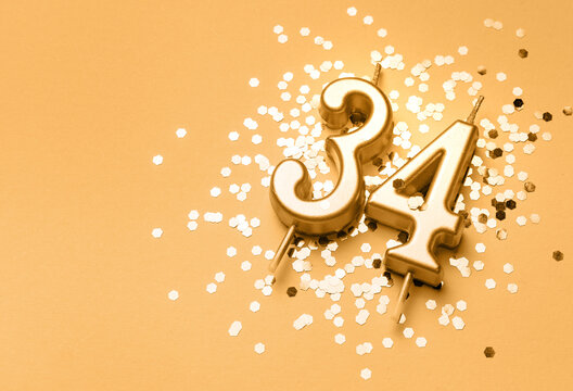 34 years birthday celebration festive background made with golden candle in the form of number Thirty four lying on sparkles. Universal holiday banner with copy space.