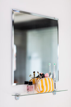 hygiene, beauty and daily routine concept - close up of cosmetic bag with make-up stuff and electric toothbrush on mirror shelf in bathroom
