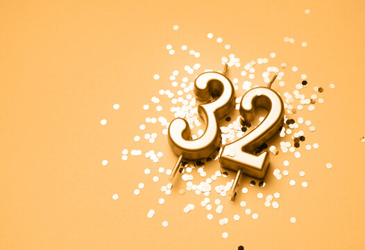 32 years birthday celebration festive background made with golden candle in the form of number Thirty two lying on sparkles. Universal holiday banner with copy space.