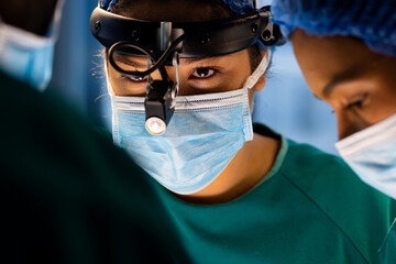Diverse male and female surgeons with face masks doing surgery in hospital operating room