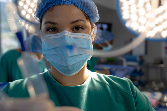 Portrait of biracial female surgeon with face mask in hospital operating room - Powered by Adobe