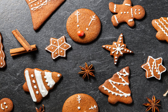 baking, cooking, christmas and food concept - close up of iced gingerbread cookies, cinnamon and star anise on black table top