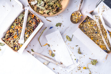 Alternative healthy herbal smoking blend. Handmade craft cigarette, preparation process, with mixture of herbs, leaves and flowers, with boxes, paper, on white background