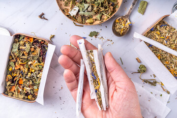 Alternative healthy herbal smoking blend. Handmade craft cigarette, preparation process, with mixture of herbs, leaves and flowers, with boxes, paper, on white background
