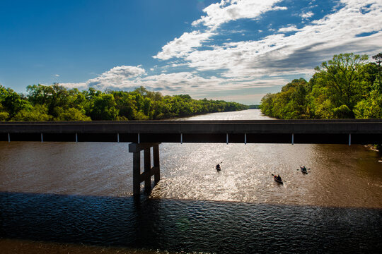 Three kayakers paddle downstream on the Cape Fear River past a bridge near Fayetteville, North Carolina