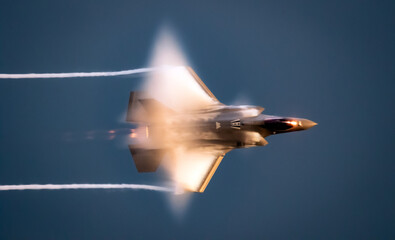 Modern American military stealth fighter jet in flight with vapor clouds during sunet.