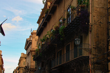 Facade of ancient building in downtown of Palermo. Balcony with flower’s pots. Typical architecture in sicilian cities. Travel and tourism concept. View of residential buildings in the medieval street
