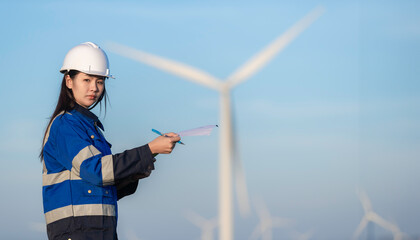 Two engineers working and holding the report at wind turbine farm Power Generator Station on mountain,Thailand people,Technician man and woman discuss about work