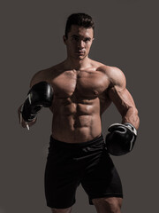 Fototapeta na wymiar A muscular young man in studio with no shirt and boxing gloves