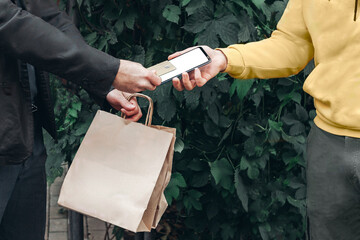 Man pays for food delivery .Male courier food delivery man in positive in uniform hands over food order and receives electronic payment card from man client in jacket. concept food delivery card payme