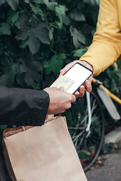 Man pays for food delivery .Male courier food delivery man in positive in uniform hands over food order and receives electronic payment card from man client in jacket. concept food delivery card