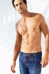 Fototapeta premium Portrait, fashion and body with a young man outdoor on a white background for masculine style. Summer, shirtless and the muscles of a confident young model in a denim jeans for health or fitness