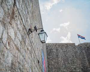 Two pigeons perched on the lantern by old grey brick walls of Dubrovnik Old Town
