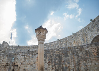Pigeons perched on very old medieval style pillar in Dubrovnik against cloudy sky
