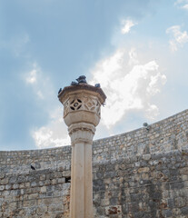 Pigeons perched on very old medieval style pillar in Dubrovnik against cloudy sky