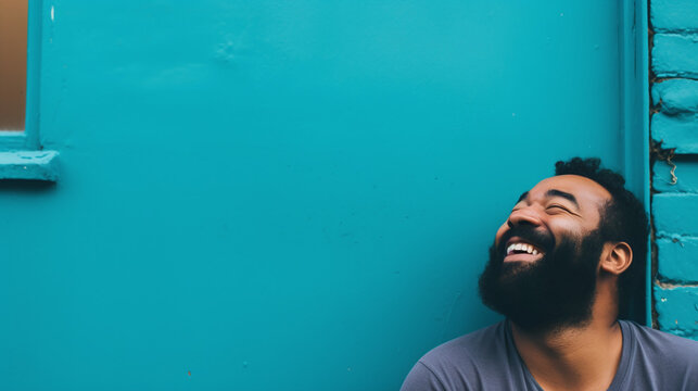 Happy Bearded Man Laughing Against Turquoise Blue Wall Background with Copy Space