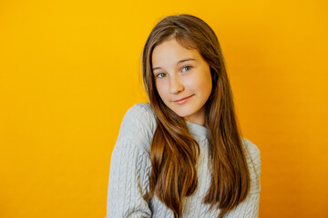 Portrait of little brunette girl who smiles sweetly at camera on yellow isolated background