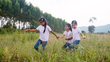 Three active sister cute child girls hold hands move way forward go walk in rural green grass...