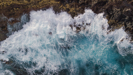 Drone view of Atlantic ocean with strong swell beating against the walls of a rocky cliff, blue...