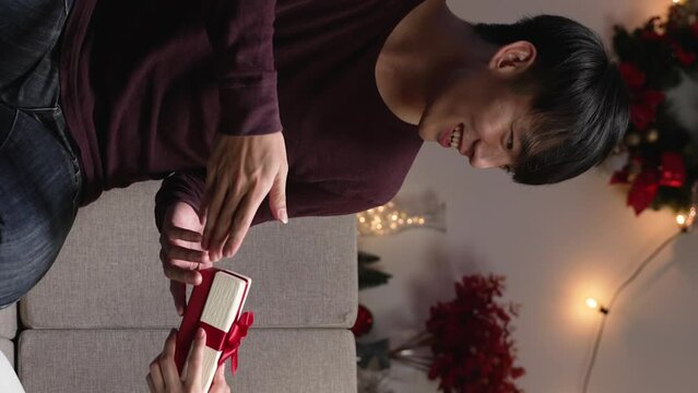 Vertical Screen: smiling asian young man giving Christmas present to girlfriend while celebrating xmas eve at home in dark night. Happy New Year.